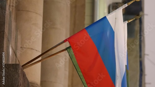 Flag of Russia on staff on building of the Federal Bailiff Service. Green flag with the coat of arms of bailiff service. Tricolor of the Russian Federation. National flag. December 24, 2019, evening.