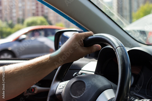 Man's hands holding steering wheel while driving car on city road.
