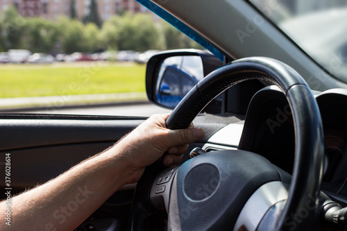 Man's hands holding steering wheel while driving car on city road.