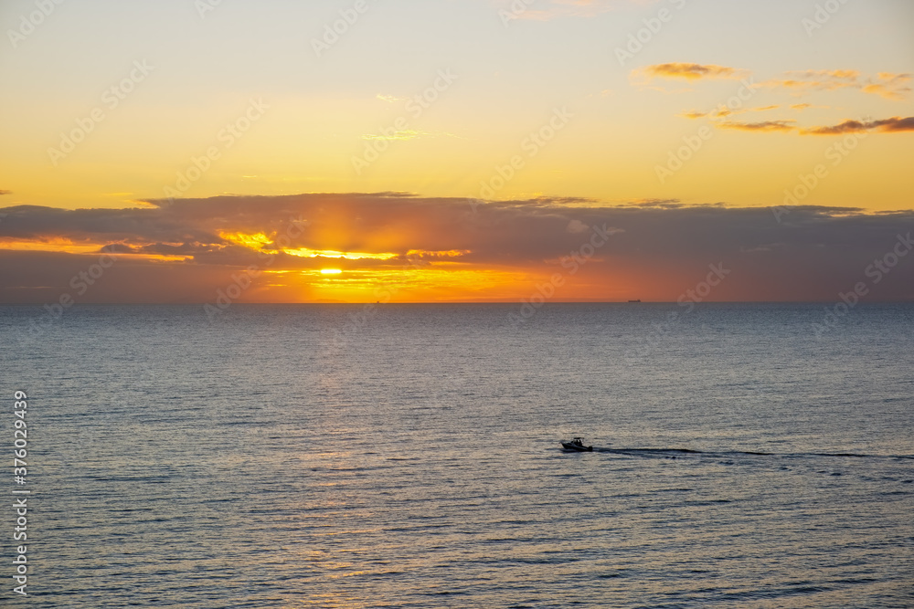 Fishing boat leaving water trail in the ocean at sunset - minimalist landscape