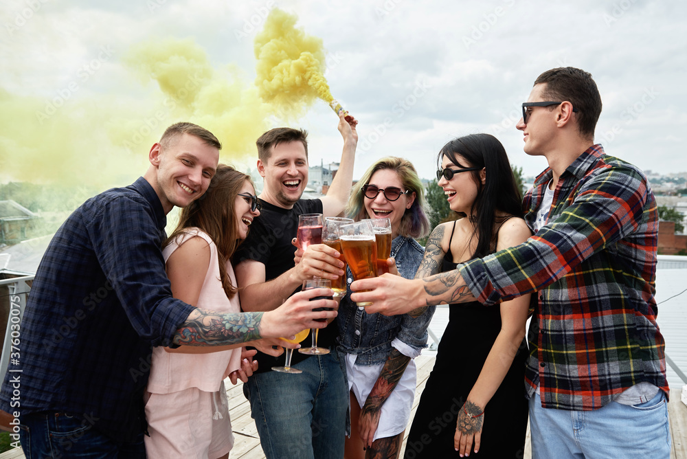 Obraz premium Group of friends drinking beer before festival at outdoors pub on roof, toasting and laughing, copy space. Friendship and celebration concept