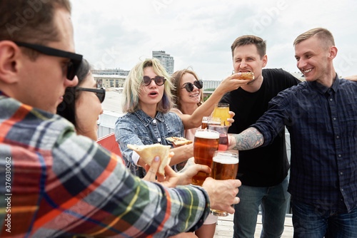 Sticker Group of friends drinking beer and eating pizza before festival at outdoors pub on roof, toasting and laughing, copy space