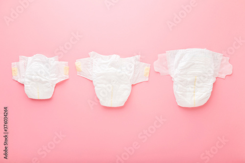 White soft baby diapers on light pink table background. Pastel color. Different sizes. Closeup. Top down view.