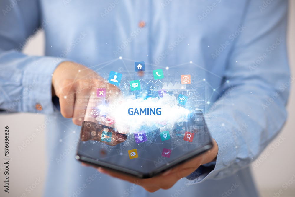 Businessman holding a foldable smartphone with GAMING inscription, technology concept Businessman holding a foldable smartphone with GAMING inscription, technology concept