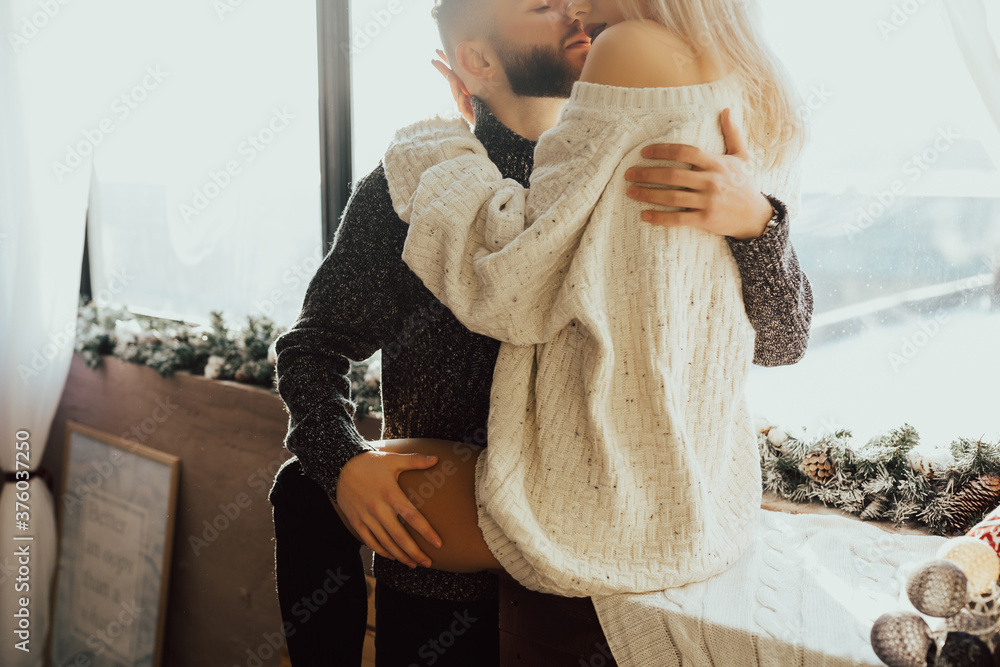 Young couple of man and woman in casual clothes, sitting on windowsill and passionately hugging. Woman and man enjoying perfect relationships