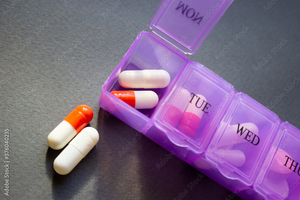 Daily pill dispenser with assorted meds on dark background. Pill box with days of the week