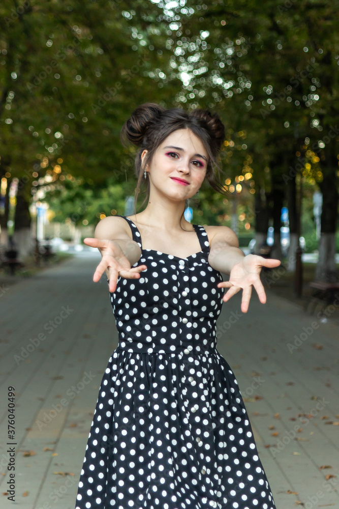 Girl in a dress with polka dots. The girl stretches her arms forward. Girl in city park