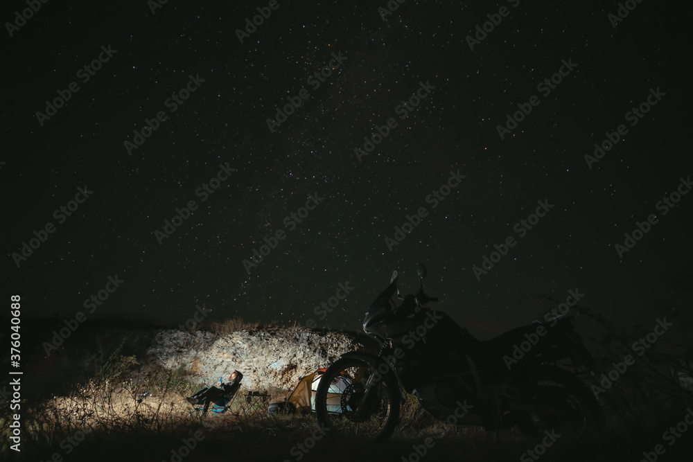 Obraz premium Night camp on the top of the mountain, Camping with tent and motorcycle, Overnight in the wild. Starry sky with the milky way. Starfall. The concept of an active lifestyle and extreme hobbies.