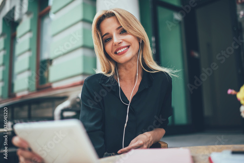 Portrait of pretty female millennial with cute smile and white teeth looking at camera spending time for music hobby, happy blonde woman in electronic headphones listening positive audio playlist