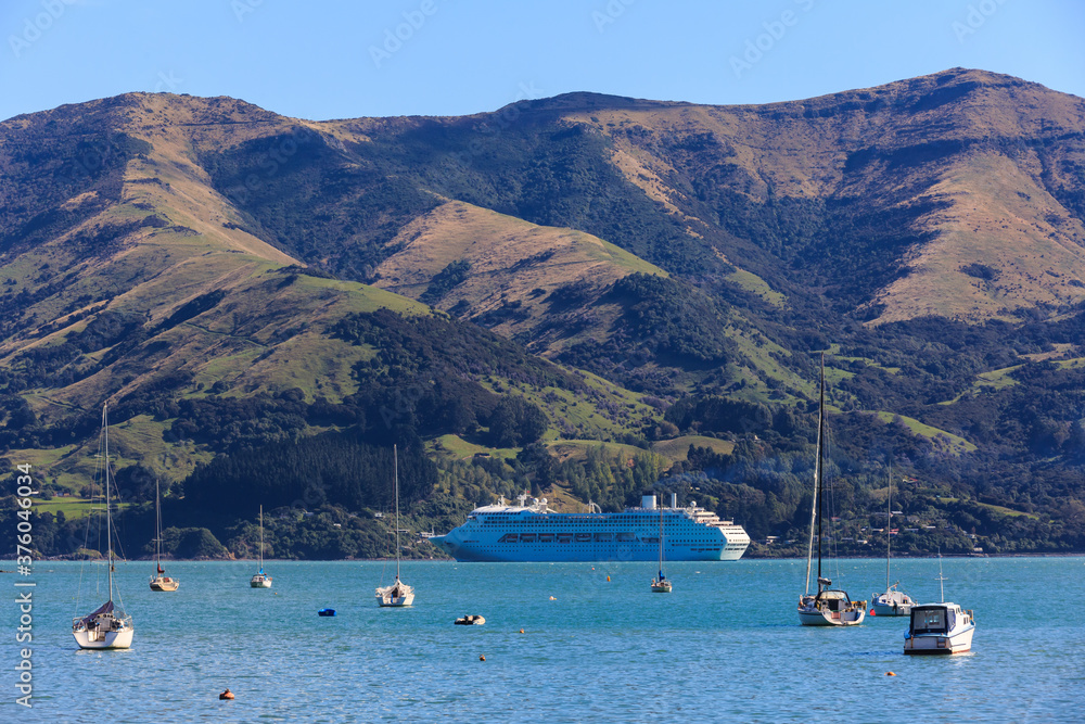 Fototapeta premium A cruise liner in Akaroa Harbour, New Zealand, surrounded by a mountainous coastline and yachts