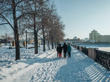 People walking on the embankment in Chelyabinsk in winter time. Alley with a trees near the river in Chelyabinsk