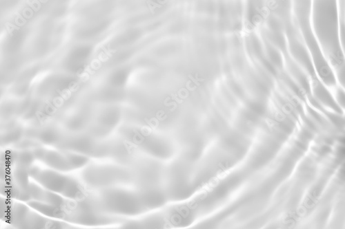 Blurred desaturated transparent clear calm water surface texture with splashes and bubbles. Trendy abstract nature background. White-grey water waves in sunlight. Copy space.
