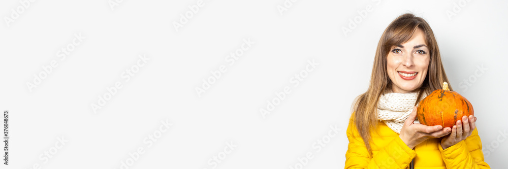 beautiful young girl in a yellow jacket holds a pumpkin on a light background. Halloween concept, autumn, celebration. Banner beautiful young girl in a yellow jacket holds a pumpkin on a light background. Halloween concept, autumn, celebration. Banner