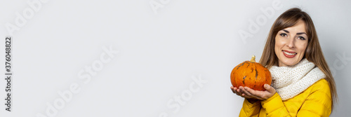 beautiful young girl in a yellow jacket holds a pumpkin on a light background. Halloween concept, autumn, celebration. Banner
