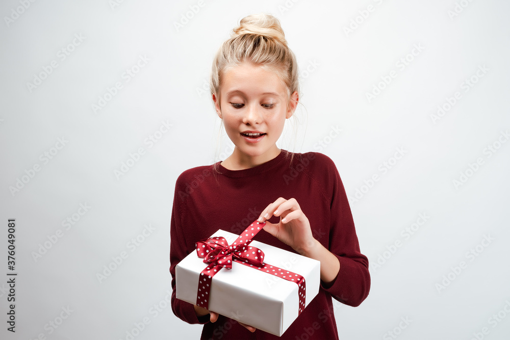 Beautiful blonde girl 10-12 years old dressed in casual sweater, holding gift box Beautiful blonde girl 10-12 years old dressed in casual sweater, holding gift box