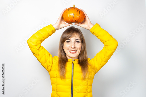 happy young girl above her head holds a pumpkin on a light background. Halloween concept  autumn  celebration