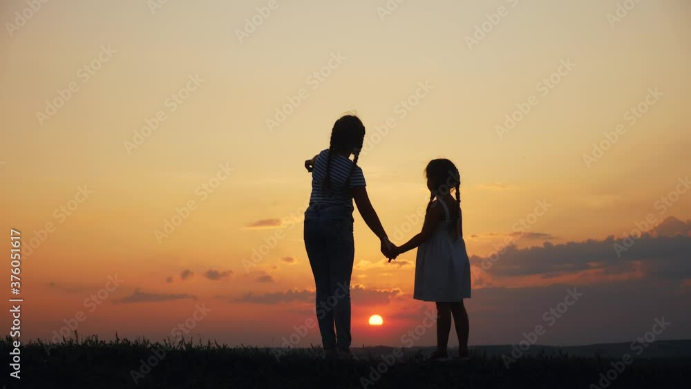 happy family two sisters walks at sunset in the park silhouette. two daughters hold hands outdoors. kid dream concept. happy family walk together. children little sunset kid walking in the park happy family two sisters walks at sunset in the park silhouette. two daughters hold hands outdoors. kid dream concept. happy family walk together. children little sunset kid walking in the park