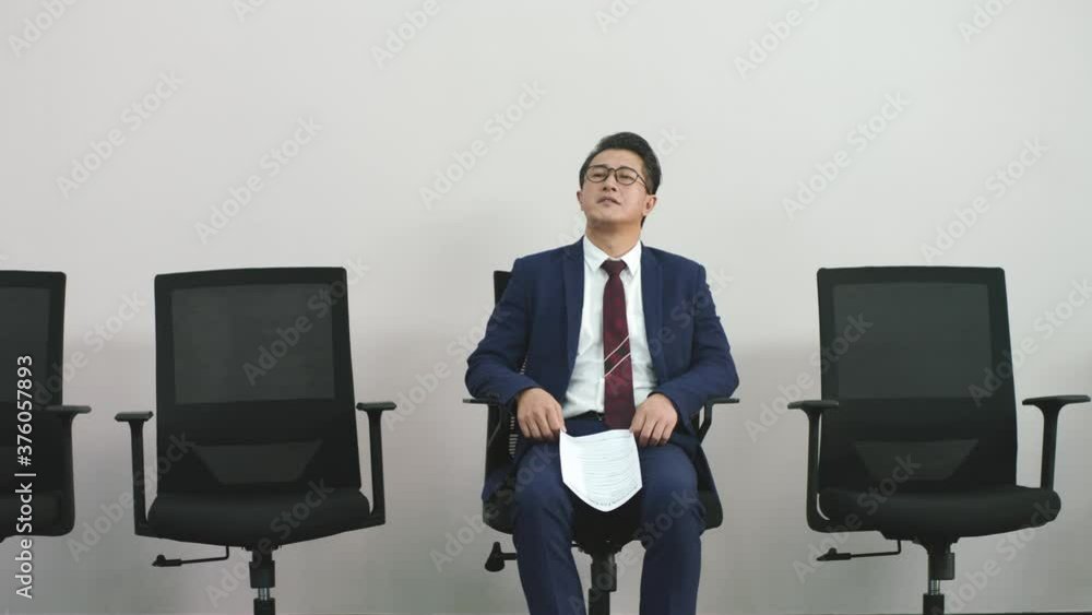 older asian business man sitting in chair waiting for his turn to be interviewed looking depressed frustrated and unsure