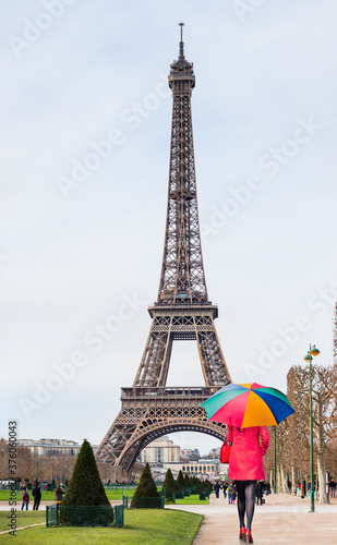 Eiffel tower in Paris - Young woman in red clothes walking on the street with multicolored umbrella