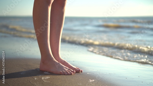 A young woman stands barefoot on the sandy seashore. Legs close up.