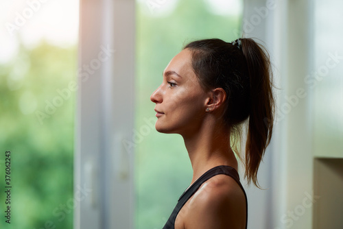 A side view photo of a sporty slim girl in a black workout tight suit is relaxing before training near the window at home. Free Download A side view photo of a sporty slim girl in a black workout tight suit is relaxing before training near the window at home. - GFXLoad