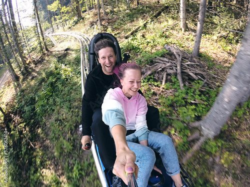 Summer toboggan run rodelbahn with many curves on a mountain. Alpine coaster in summer and autumn beautiful landscapes. Fast ride fun of young couple travelling