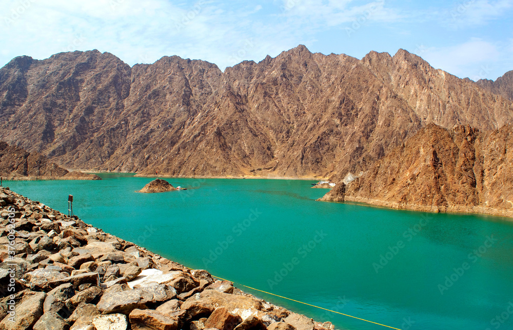 Beautiful deep green Hatta lake with rocky Hajar Mountains on background. Overview of Hatta dam in UAE, Oman. Picturesque nature in the Middle East.