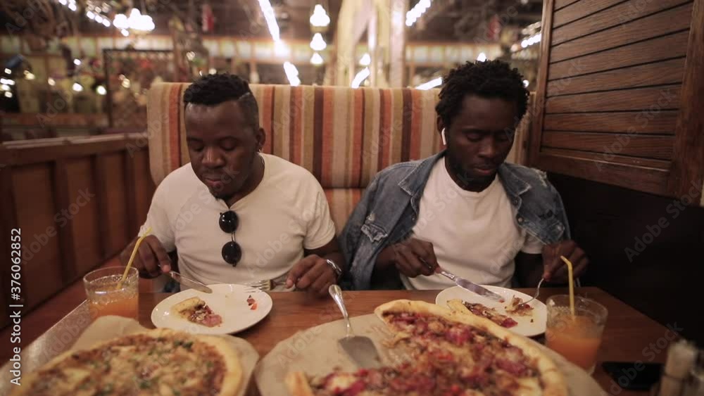 African men friends eating pizza in restaurant African men friends eating pizza in restaurant