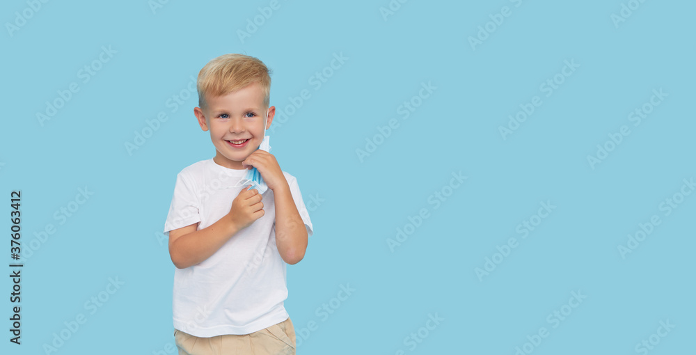 End of quarantine. Portrait of cute little child boy removes the protective medical mask from the face on blue background. Virus protection and healthcare concept. End of quarantine. Portrait of cute little child boy removes the protective medical mask from the face on blue background. Virus protection and healthcare concept.