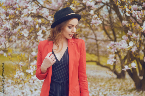 A girl in autumn clothes, in a red jacket and hat on a background of a tree with falling leaves