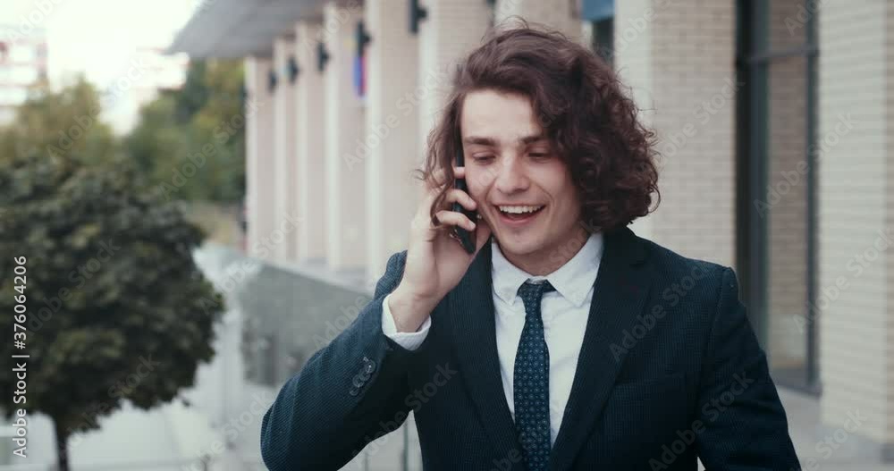 Close up of successful handsome young businessman standing outdoors talking on cellphone to client, having friendly conversation, pleasant phone call, enjoying work, looking cheerful and surprised. Close up of successful handsome young businessman standing outdoors talking on cellphone to client, having friendly conversation, pleasant phone call, enjoying work, looking cheerful and surprised.