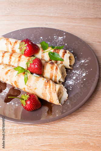 Pancakes with banana and strawberries on a plate. Banana wrapped in a pancake and with strawberries on top. Breakfast with Pancakes with berries and banana and chocolate..