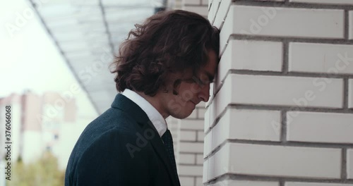 Angry nervous young businessman corporate worker banging his head against the wall in despair. Frustrated man entrepreneur looking worried about project loss.