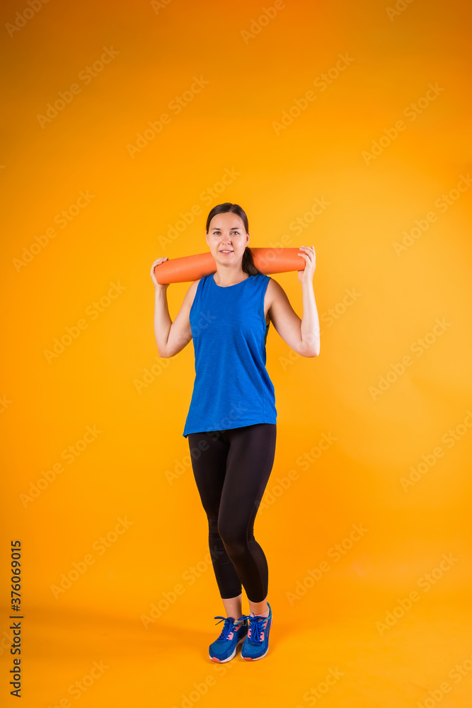 A full-length sportswoman with an orange Mat and looks at the camera on an orange background. A full-length sportswoman with an orange Mat and looks at the camera on an orange background.