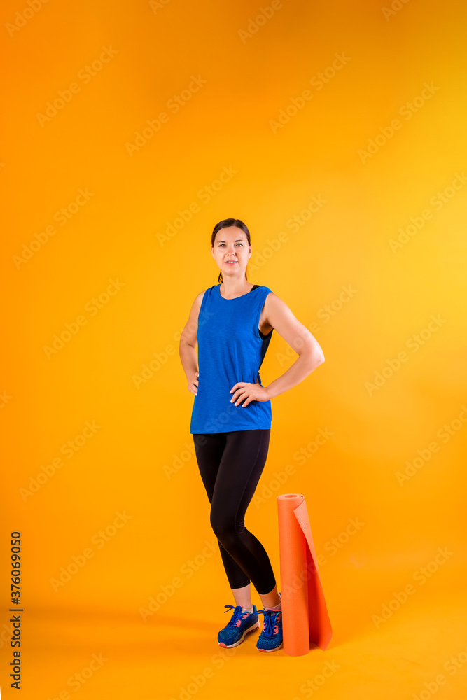 Full-length sporty girl with a fitness Mat on an orange background