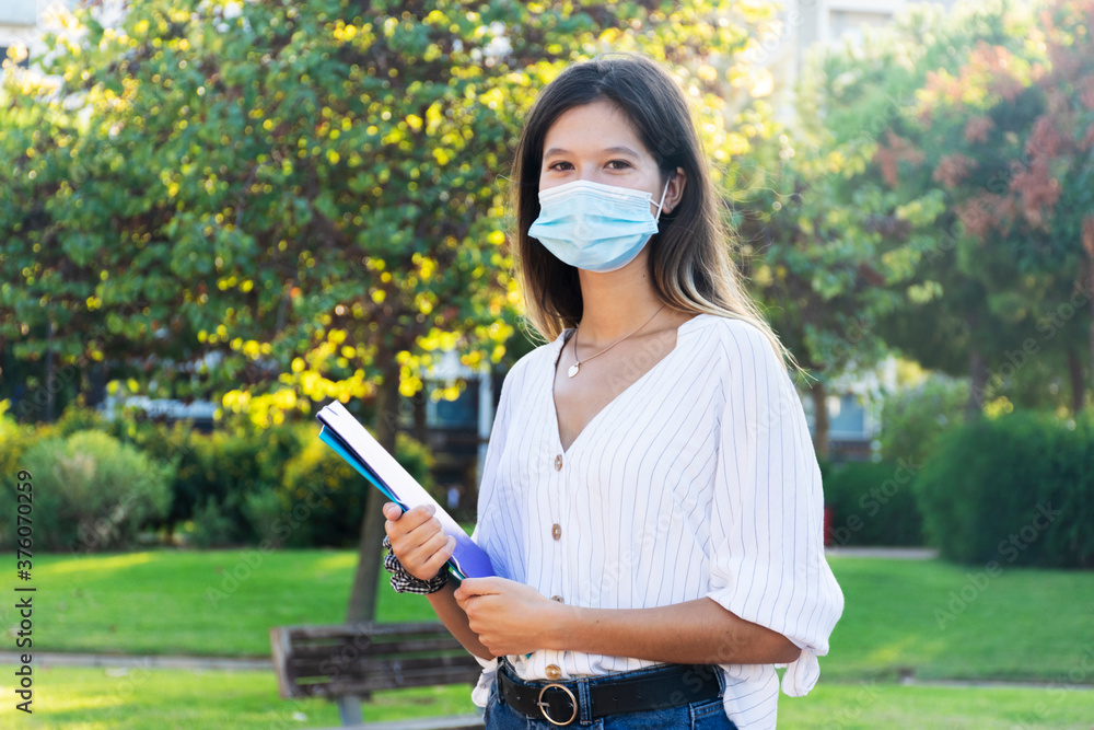 Young woman wearing a medical mask and holding folders at the park campus Young woman wearing a medical mask and holding folders at the park campus