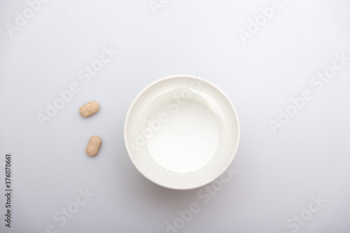 An Asian hand holding two pills and a paper cup filled with water