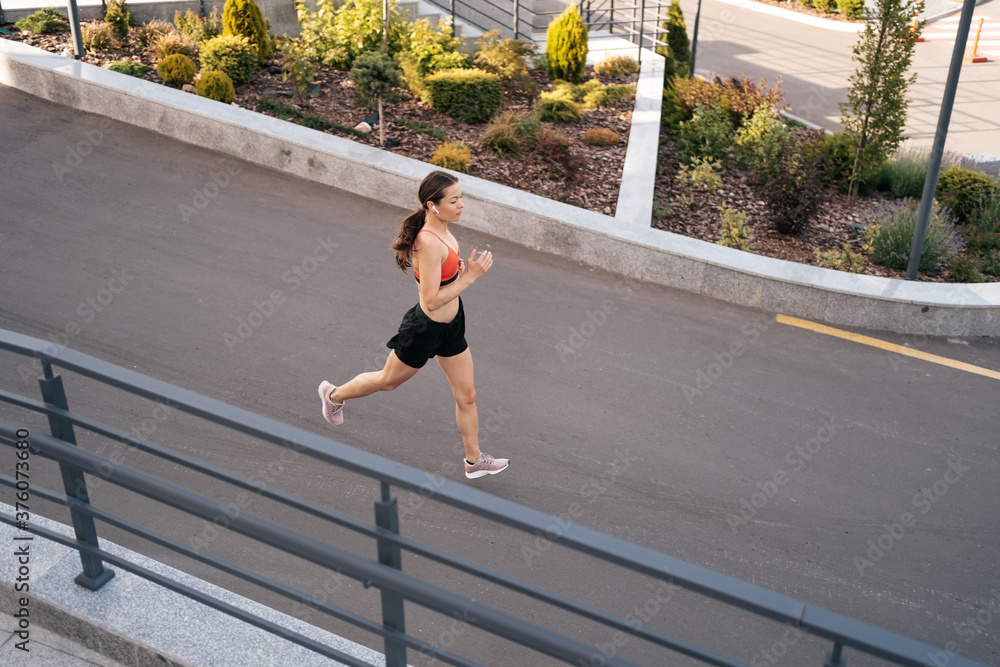 Fototapeta premium Young woman sprinting in the morning outdoors. Side view of female runner working out in the city.