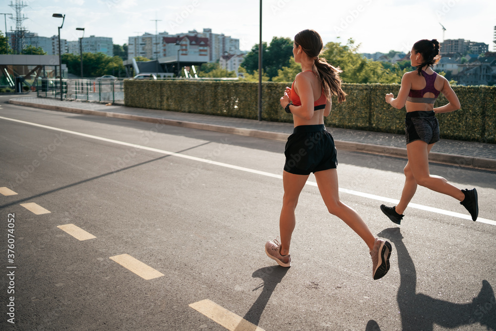 Young woman running on sidewalk in morning. Health conscious concept. Healthy active lifestyle. Active girls jogging together on road in the city.