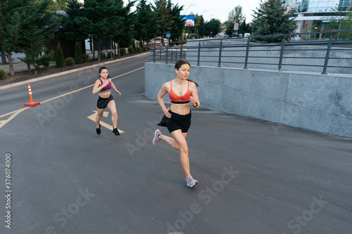 Young woman running on sidewalk in morning. Health conscious concept. Healthy active lifestyle. Active girls jogging together on road in the city.