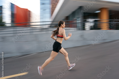 Young woman sprinting in the morning outdoors. Side view of female runner in motion working out in the city.