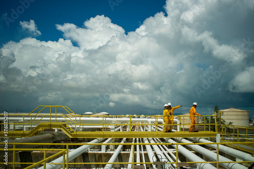 Multi-Ethnic female and male industry engineers in protective clothing hart hat walking on a walkway bridge over petrochemical refinery plant pipelines. Successful African Chinese oil gas cooperation.