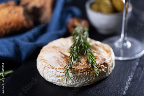 Camembert cheese with rosemary, olives and rustic bread on a dark background photo