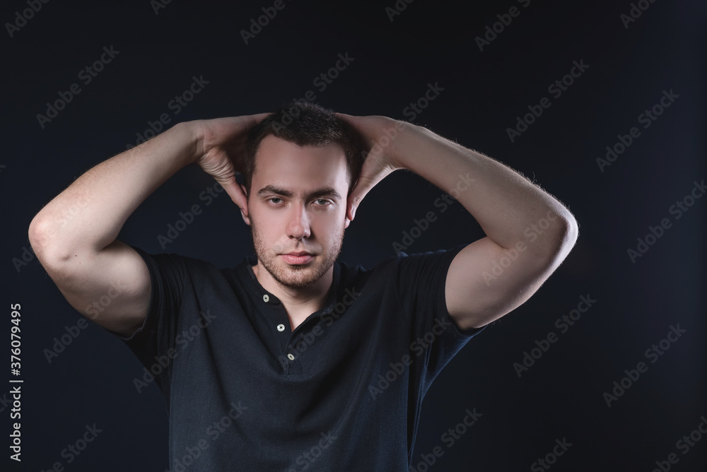 Handsome young man in a black polo shirt holding his head on a dark background in the studio Handsome young man in a black polo shirt holding his head on a dark background in the studio
