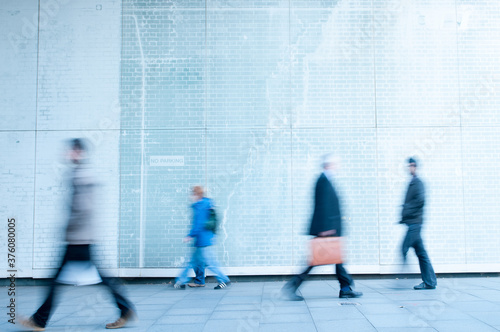 Motion blurred image of people walking against a light coloured wall