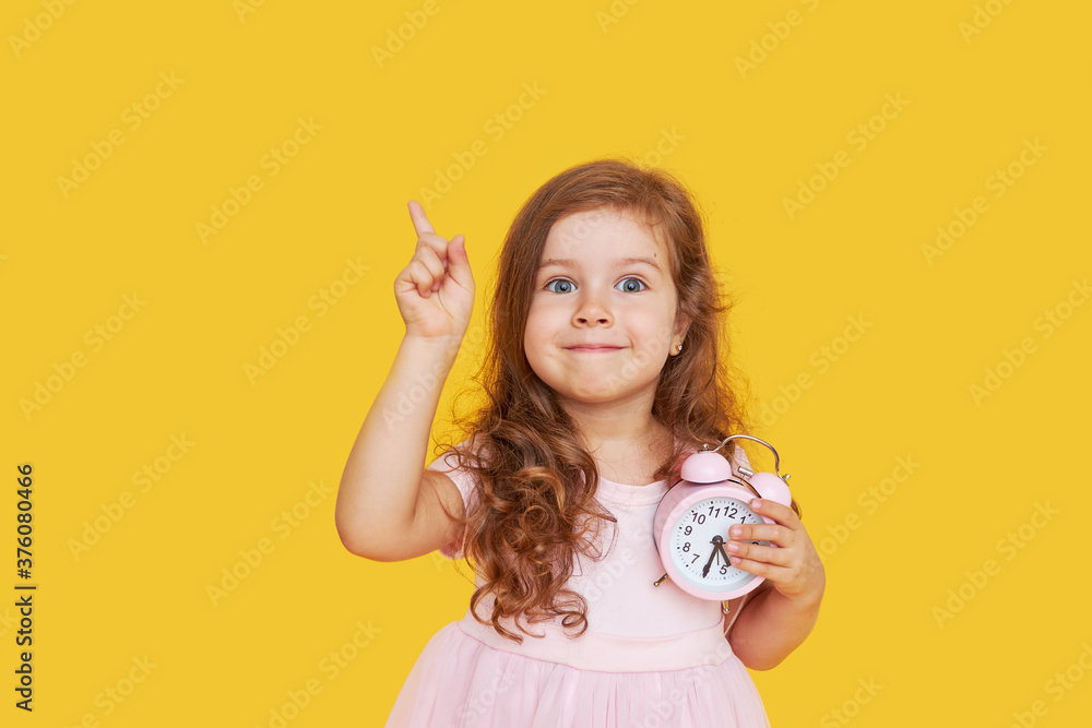 Time for a party. A pensive cute child in a fancy dress holds a small alarm  clock in his hands and shows up. Yellow studio background.. Stock Photo |  Adobe Stock