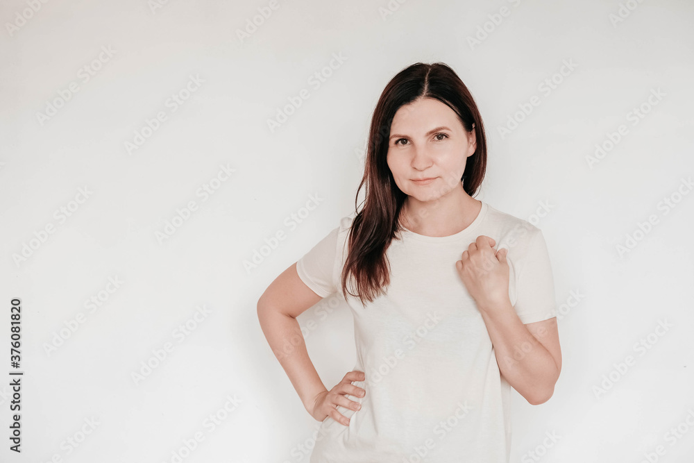 Beautiful brunette woman keeps hands on cheek, dressed in casual white t shirt, has minimal makeup, poses indoor on a white background. Copy, empty space for text Beautiful brunette woman keeps hands on cheek, dressed in casual white t shirt, has minimal makeup, poses indoor on a white background. Copy, empty space for text