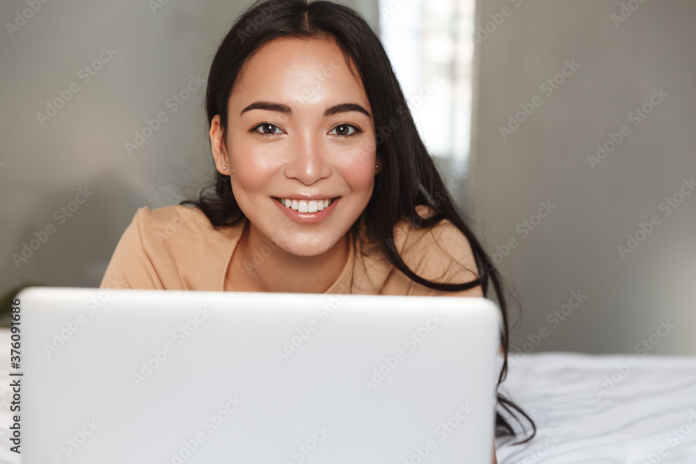 Close-up of beautiful young asian girl lying in bed and using laptop, looking happy and relaxed. Woman spend time at home in comfort, shopping online or working remote with computer Close-up of beautiful young asian girl lying in bed and using laptop, looking happy and relaxed. Woman spend time at home in comfort, shopping online or working remote with computer