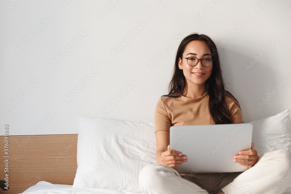 Young ambitious asian woman working remote from home, sit comfortable on bed and using laptop. Female freelancer writing texts or watching online webinars in her bedroom. Girl with computer smiling Young ambitious asian woman working remote from home, sit comfortable on bed and using laptop. Female freelancer writing texts or watching online webinars in her bedroom. Girl with computer smiling