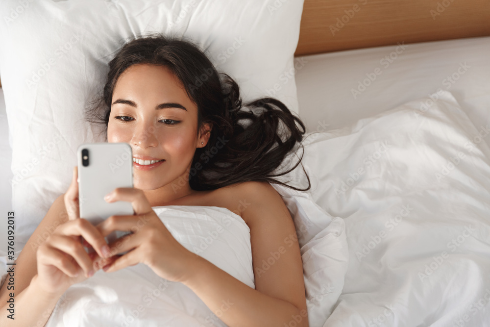 Lifestyle, leisure and lazy mornings concept. Close-up high angle of beautiful asian girl checking messages on smartphone while lying in bed. Woman browsing social networks after waking-up Lifestyle, leisure and lazy mornings concept. Close-up high angle of beautiful asian girl checking messages on smartphone while lying in bed. Woman browsing social networks after waking-up